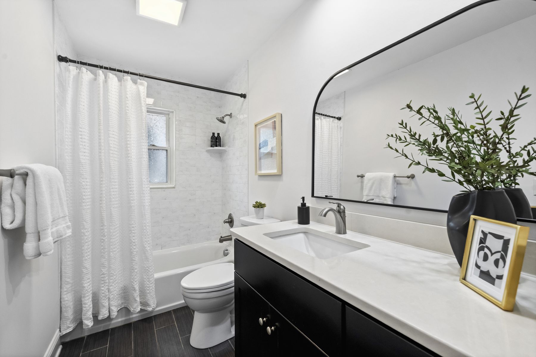 Renovated full bath with a black stone-topped vanity and a subway-tiled tub and shower